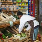 Grocery store worker arranging fresh vegetables in a market display.